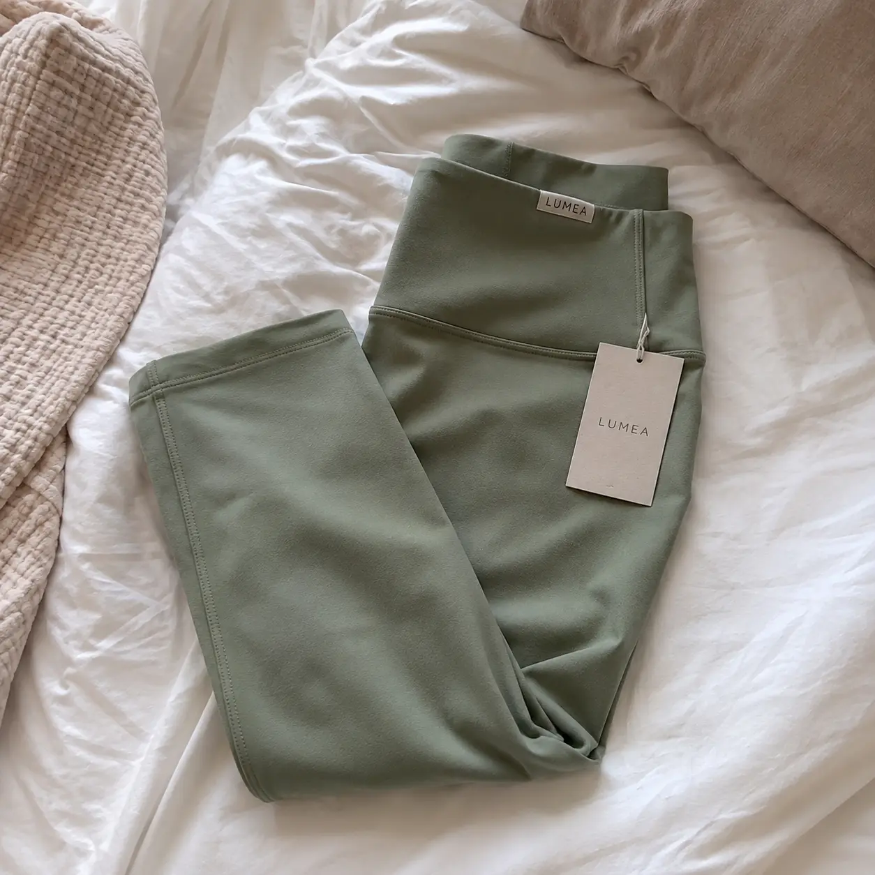 Phone photo of folded sage green leggings on rumpled bedding