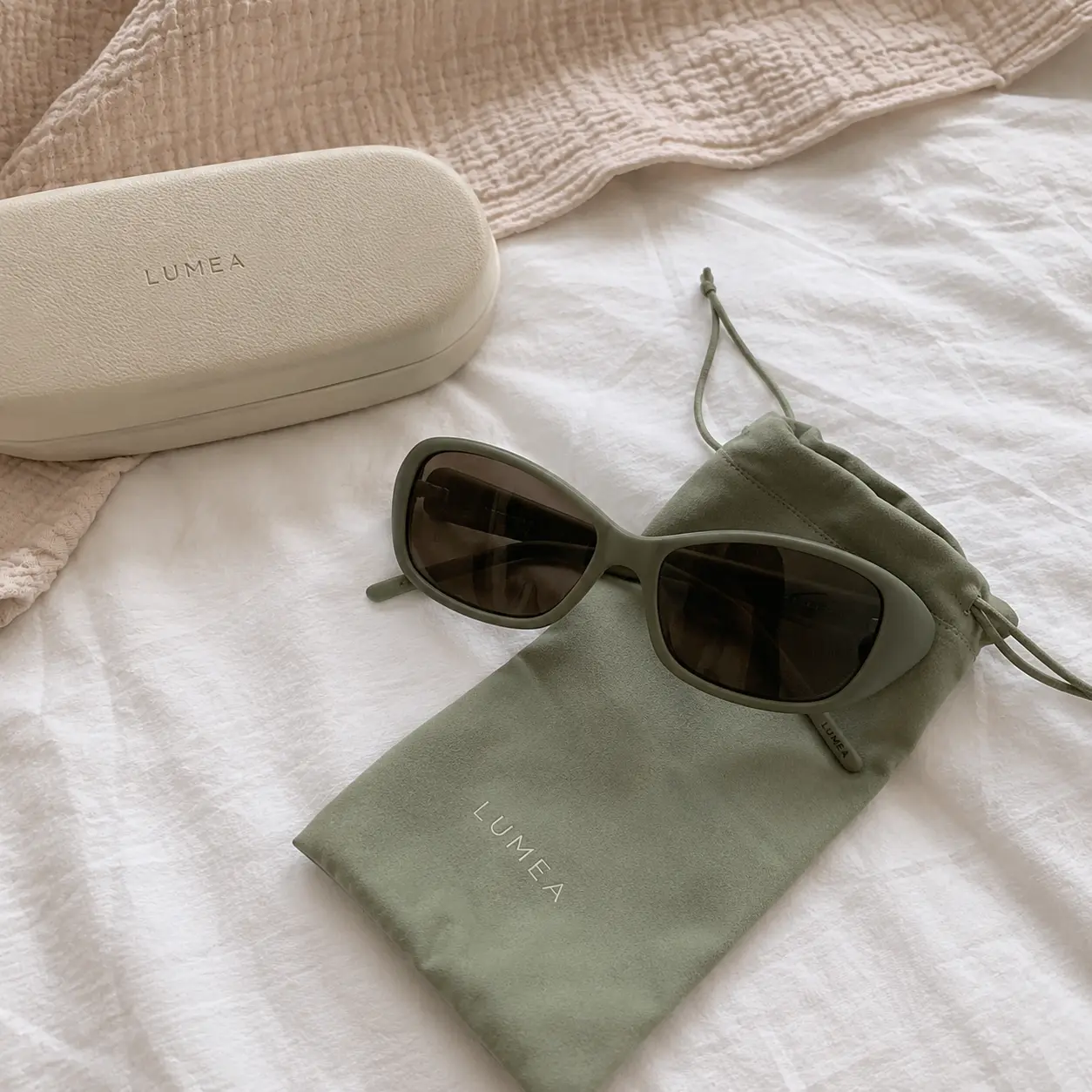 Phone photo of sunglasses and a suede pouch on white bedding