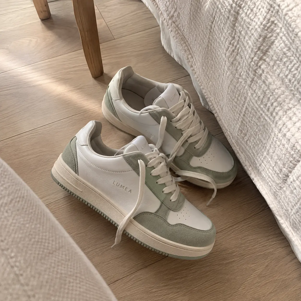 Phone photo of white and sage sneakers on a wooden floor